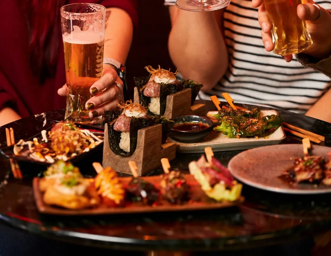 Mesa compartida con brochetas y cervezas en Ichiba